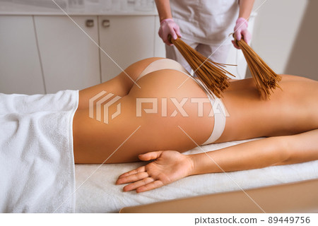 Woman masseuse doing double samurai massage with bamboo brooms in spa. Woman masseuse doing double samurai massage with bamboo brooms in spa. 89449756