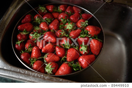 Juicy ripe red strawberries are washed in a steel bowl full of water. 89449910