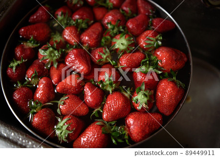 Juicy ripe red strawberries are washed in a steel bowl full of water. 89449911