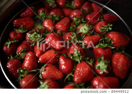 Juicy ripe red strawberries are washed in a steel bowl full of water. 89449912