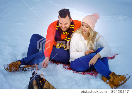 happy couple man and woman in winter in the forest fry marshmallows on the fire 89450347