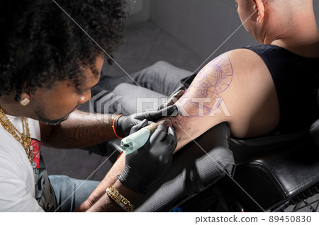 Professional African American tattoo artist makes a tattoo on client arm Professional African American tattoo artist makes a tattoo on client arm 89450830