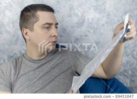 Man on a white background reads the instructions for medicines. Male looks at the list and composition of the drug. The concept of home self-medication and the study of the properties of drugs 89451047