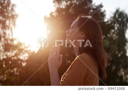 Peaceful woman holds her palms in front her in prayer against backdrop trees 89451088