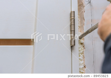 Carpenter at installing interior wood door installation working with mounting foam 89453823