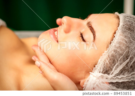 Facial massage. Hands of a masseur massaging neck of a young caucasian woman in a spa salon, the concept of health massage 89453851