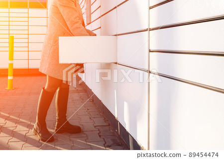 Pickup parcel. Courier box in woman hands at post delivery automat terminal. Self service post terminal and parcel delivery concept. 89454474