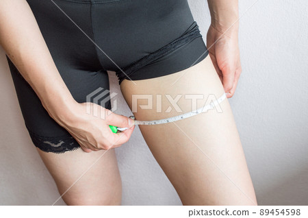 Athletic slim woman measuring her legs by measure tape. Body care and slim concept. Athletic slim woman measuring her legs by measure tape. Body care and slim concept. 89454598