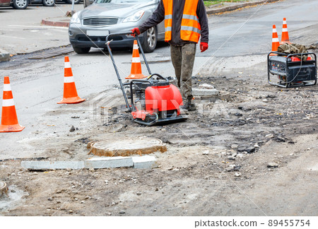 A road service worker repairs a section of the carriageway near a sewer manhole. 89455754