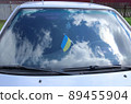 The Ukrainian flag is affixed to the windshield of a car. Reflected sky with clouds. 89455904