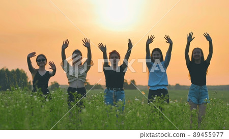 Girls friends waving their hands to the setting sun on the background of the sunset. Girls friends waving their hands to the setting sun on the background of the sunset. 89455977