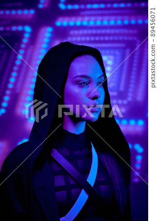 Serious attractive female video game character in hood standing against luminous background 89456071