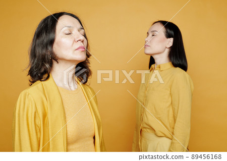 Calm multi-ethnic women with closed eyes standing against yellow background and raising heads Calm multi-ethnic women with closed eyes standing against yellow background and raising heads 89456168
