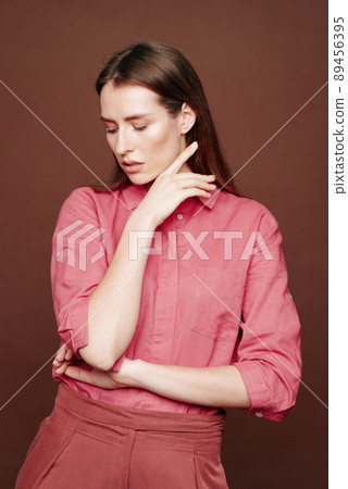 Vulnerable young woman in dark pink blouse demonstrating her weakness while posing against isolated background 89456395
