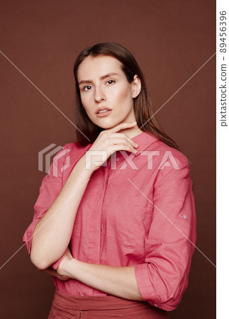 Portrait of tender young woman with slowly opened mouth touching her neck against brown background 89456396
