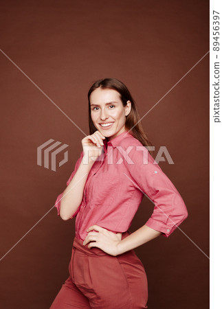 Portrait of cheerful confident young lady in pink shirt touching chin against brown background 89456397
