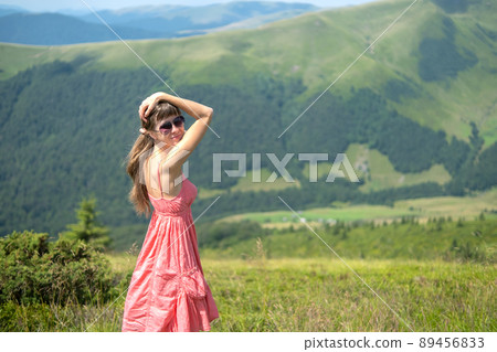 Young woman in red dress standing on grassy field on a windy day in summer mountains enjoying view of nature. Young woman in red dress standing on grassy field on a windy day in summer mountains enjoying view of nature. 89456833