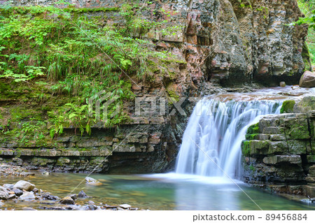 Waterfall on mountain river with white foamy water falling down from rocky formation in summer forest. Waterfall on mountain river with white foamy water falling down from rocky formation in summer forest. 89456884