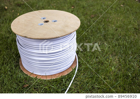 Top view of roll of white industrial electrical cable on large wooden reel isolated outdoors on green grass. Professional construction site cable, reliable wiring and durability. Top view of roll of white industrial electrical cable on large wooden reel isolated outdoors on green grass. Professional construction site cable, reliable wiring and durability. 89456910