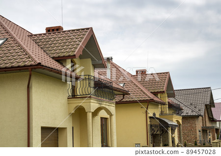 New yellow two-story residential cottage with shingle roof, front porch, plastic windows, high chimneys, balconies on blue sky background. Real estate property, architecture and prosperity concept. New yellow two-story residential cottage with shingle roof, front porch, plastic windows, high chimneys, balconies on blue sky background. Real estate property, architecture and prosperity concept. 89457028