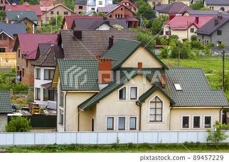 Close-up of big new comfortable two-storied new cottage with green tile roof, big yard, plastic windows and high chimneys in modern quiet suburban residential area. Perfect investment in dream house. Close-up of big new comfortable two-storied new cottage with green tile roof, big yard, plastic windows and high chimneys in modern quiet suburban residential area. Perfect investment in dream house. 89457229