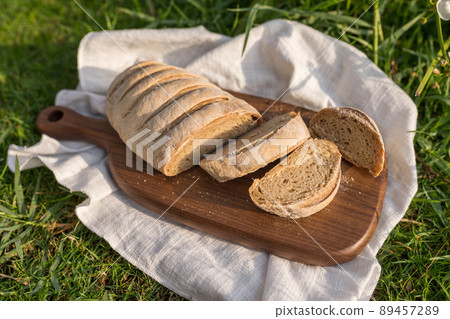 Composition of homemade white flour bread on wood board with white cloth napkin on the green grass . High quality photo 89457289