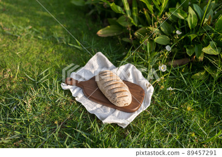 Composition of homemade white flour bread on wood board with white cloth napkin on the green grass . High quality photo 89457291