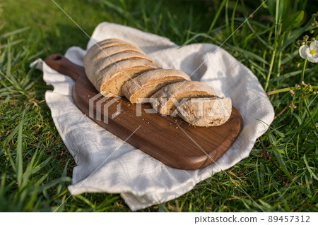 Composition of homemade white flour bread on wood board with white cloth napkin on the green grass . High quality photo 89457312