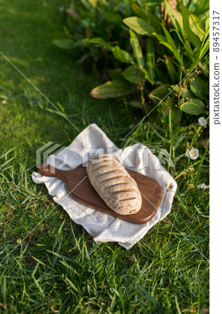Composition of homemade white flour bread on wood board with white cloth napkin on the green grass . High quality photo Composition of homemade white flour bread on wood board with white cloth napkin on the green grass . High quality photo 89457317
