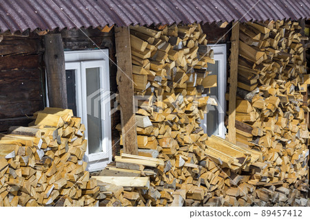 Chopped dry trunks wood outdoor at old wooden peasant house with slut roof walls on bright cold winter sunny day. Fire wood logs prepared for winter, ready for burning. Rural lifestyle concept. 89457412