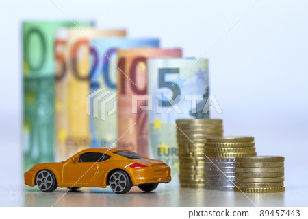 Blurred row of rolled hundred, fifty, twenty, ten and five new euro banknotes and pile of coins with yellow toy expensive sport car. Symbol of financial prosperity, vehicle sale and purchase. 89457443