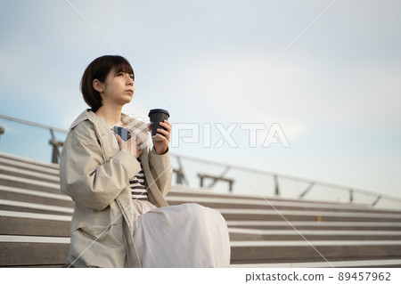 A woman sitting on the stairs with a smartphone and coffee in her hand A woman sitting on the stairs with a smartphone and coffee in her hand 89457962