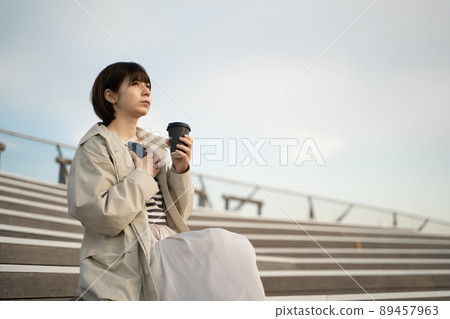 一個女人坐在樓梯上,手裡拿著智能手機和咖啡 一個女人坐在樓梯上,手裡拿著智能手機和咖啡 89457963
