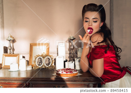 Pretty pin-up girl eats cake in retro interior. Temptation concept Pretty pin-up girl eats cake in retro interior. Temptation concept 89458415
