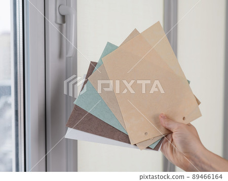Woman holding fabric samples of roller blinds against window background. Woman holding fabric samples of roller blinds against window background. 89466164