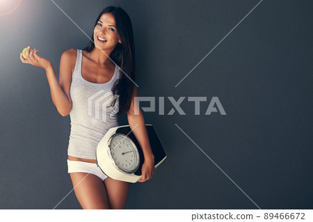Eat well and be healthy. Shot of a young woman holding an apple and scale. Eat well and be healthy. Shot of a young woman holding an apple and scale. 89466672
