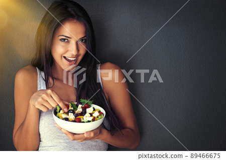 Does the body good. Portrait of a healthy young woman eating a salad against a gray background. Does the body good. Portrait of a healthy young woman eating a salad against a gray background. 89466675