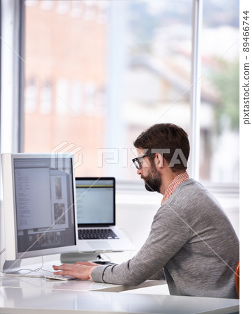 Working on the next big thing. Shot of a handsome young man working on a computer in a casual working environment. Working on the next big thing. Shot of a handsome young man working on a computer in a casual working environment. 89466744