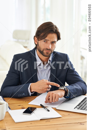 Punctuality is crucial in this office. A handsome businessman pointing to his watch while at his desk. 89466988