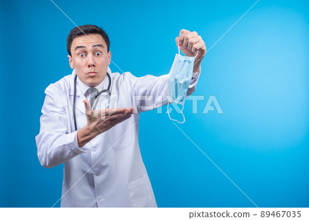 Shocked doctor pointing at protective mask in hand 89467035