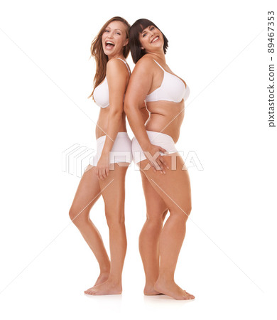 Celebrating their natural figures. Two women of different body shapes standing together back to back while isolated on white. 89467353