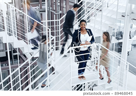 Busy making success happen. Portrait of a young professional standing on a stairs with colleagues rushing around her. 89468045