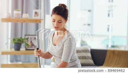 I clean because I feel happier in a clean house. Cropped shot of a young woman mopping the floor in her living room. 89469462