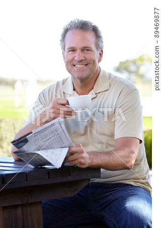 No mornings complete without coffee and a paper. Portrait of a mature man enjoying a cup of coffee outside while reading a newspaper. No mornings complete without coffee and a paper. Portrait of a mature man enjoying a cup of coffee outside while reading a newspaper. 89469877