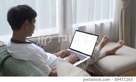Side view casual asian man resting on couch at home and using computer laptop. Side view casual asian man resting on couch at home and using computer laptop. 89471163