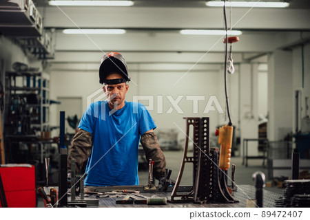 Portrait of Young Professional Heavy Industry Engineer. Worker Wearing Safety Vest and Hardhat Smiling on Camera. In the Background Unfocused Large Industrial Factory Portrait of Young Professional Heavy Industry Engineer. Worker Wearing Safety Vest and Hardhat Smiling on Camera. In the Background Unfocused Large Industrial Factory 89472407