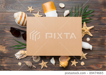 Summer time concept with blank greeting card and blank craft paper on colored background. Seashells from ocean shore in the shape of frame separated with space for text top view 89474665