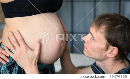 Closeup of Father Touching Pregnant Belly of his Wife at Home, Slow Motion. Young Family Waiting for the Baby Closeup of Father Touching Pregnant Belly of his Wife at Home, Slow Motion. Young Family Waiting for the Baby 89476289
