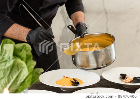 chef prepares carrot cream soup with seafood in a restaurant 89476406