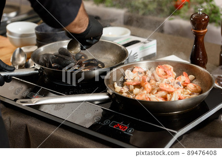 two pans with mussels and shrimp on an induction stove 89476408